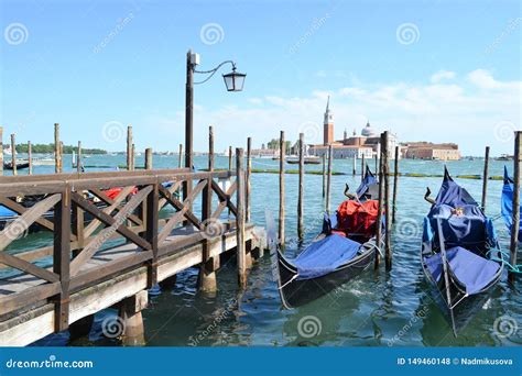 Two Gondolas Anchored At Wooden Poles Near Wooden Pier In Venice Italy