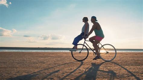 Young Woman And Man Riding A Bicycle At The Shore And Having Some Fun Slow Motion Stock Video