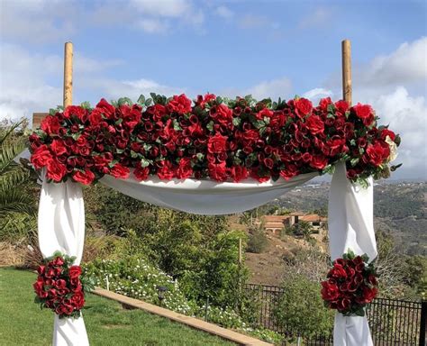 A Wedding Arch Decorated With Red Flowers And Greenery