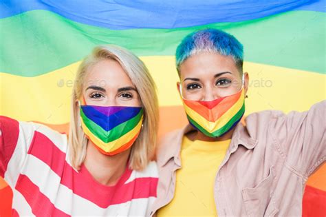 Cheerful Lesbian Women With Lgbt Rainbow Flag At Gay Pride Parade Wearing Protective Face Mask