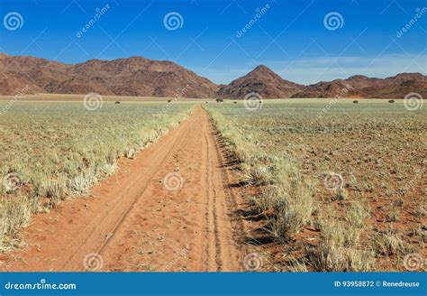 Desert Dirt Road Curving Towards Mountain Under A Blue Sky With White