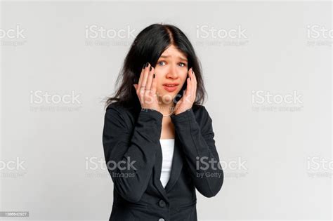 Portrait Of Startled Young Brunette Woman Grabbing Head With Both Hands In Despair Staring