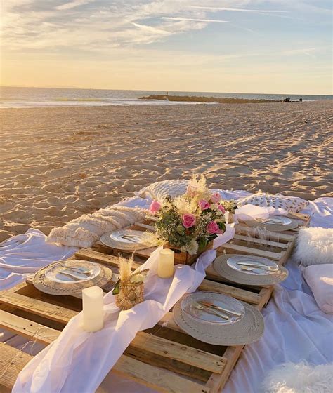 A Table Set Up On The Beach With Plates And Flowers In Vases Napkins And Candles