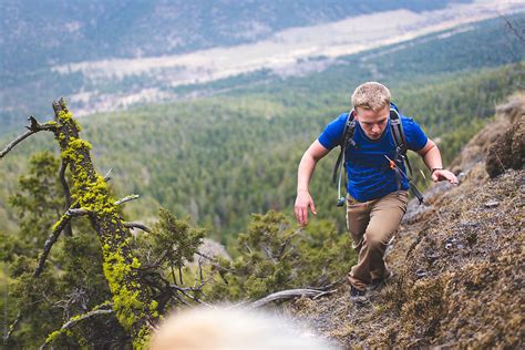 Young Man Climbing Up Steep Hill On A Mountain Overlooking A Forest