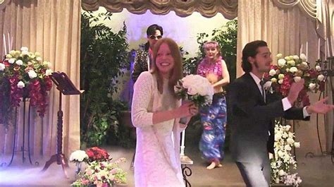 A Man And Woman Are Walking Down The Aisle With Flowers In Their Hands As People Look On