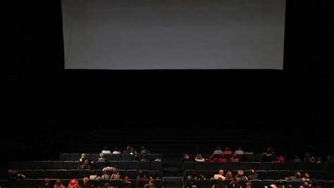 Back View Of Audience In Dark Cinema Hall In Front Of Big Blank Screen