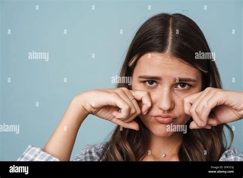 Close Up Of An Upset Cute Girl Wiping Tears Isolated Over Blue