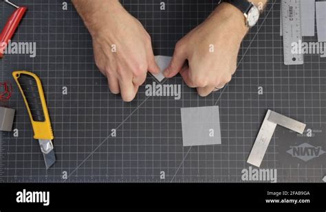 Overhead View Of Persons Hands Folding A Piece Of Paper On A Black