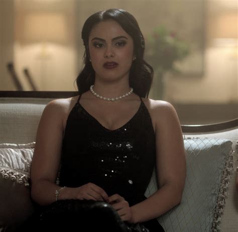 A Woman Sitting On Top Of A Couch Wearing A Black Dress And Pearl Necklaces