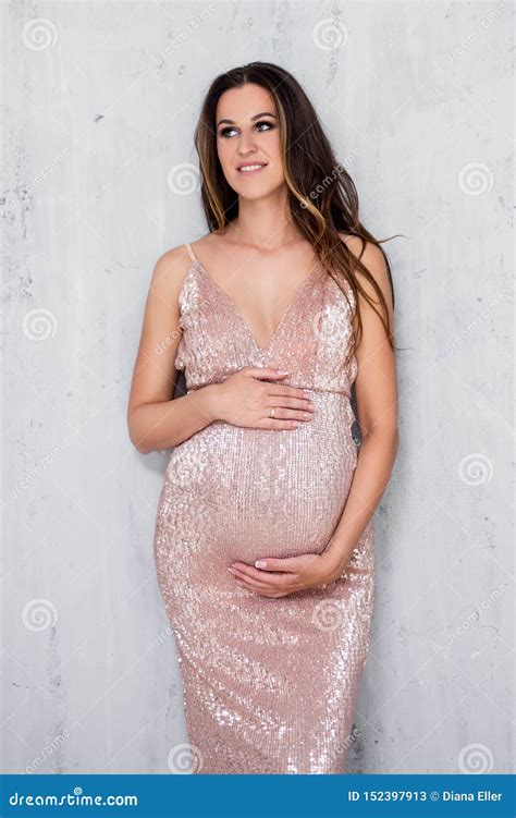 Beautiful Pregnant Woman In Shiny Evening Dress Posing Over Gray Wall