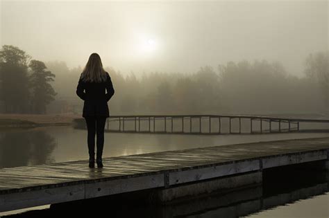 Young Woman Standing Alone On Lake Footbridge And Staring At Sunrise In