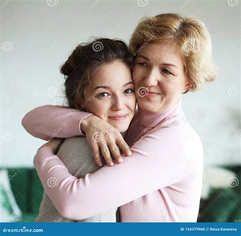 Beautiful Senior Mom And Her Adult Daughter Are Hugging Looking At Camera And Smiling At Home