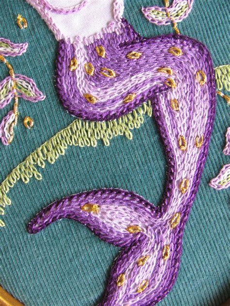 A Close Up Of A Purple And Green Embroidered Design On A Blue Cloth