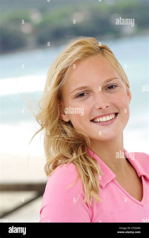 Female With Long Blonde Hair Wearing A Pink Top And Natural Make Up Smiling At The Camera Sea