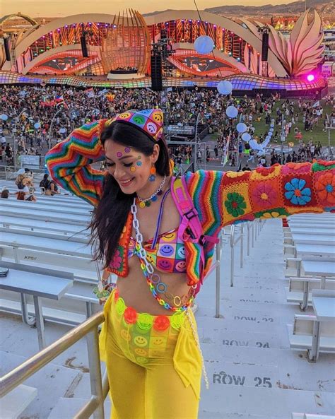 a woman in yellow pants and a colorful top at a music festival with her arms stretched out