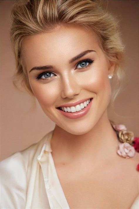 A Beautiful Woman With Blue Eyes And Blonde Hair Wearing A White Blouse Smiling At The Camera