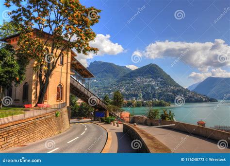 Lugano Lake Surrounded By Mountains Covered In Greenery And Buildings