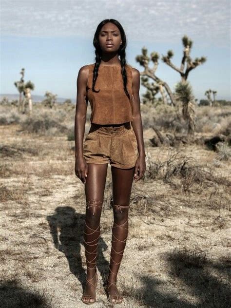 a woman standing in the middle of a desert wearing brown shorts and knee high boots