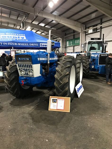 Two Large Blue Tractors Are Parked In A Warehouse With People Looking