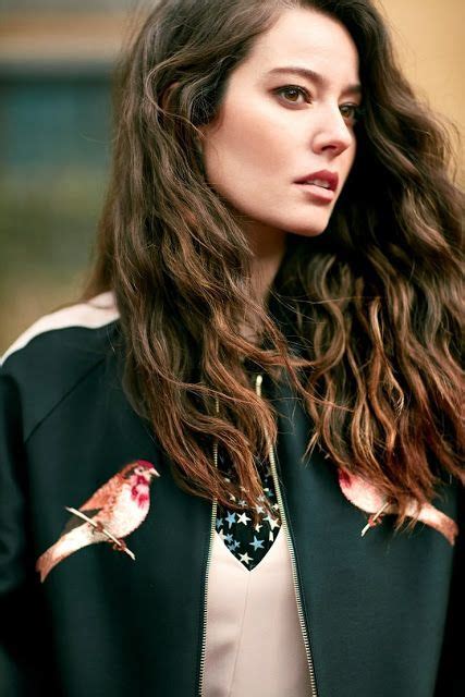 A Woman With Long Brown Hair Wearing A Black Jacket And White Top Is