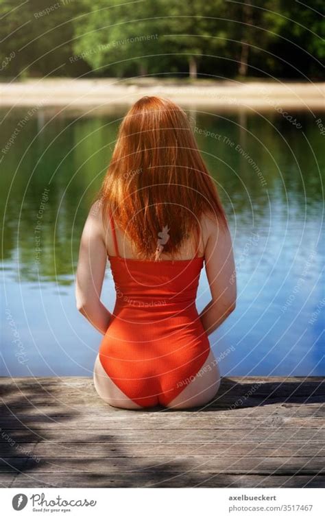 Rear View Woman Wearing Red Bathing Suit Sitting On Wooden Pier A Royalty Free Stock Photo
