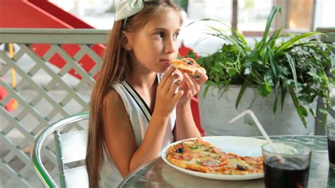 Little Girl Eating Pizza In A Fast Food Restaurant Outdoors Stock