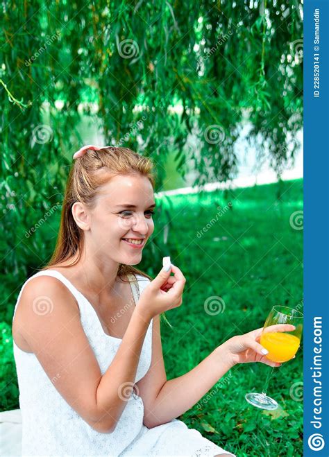Young Girl With Hair Bow In A White Dress And Sneakers Eating Sweets And Drink Orange Juice