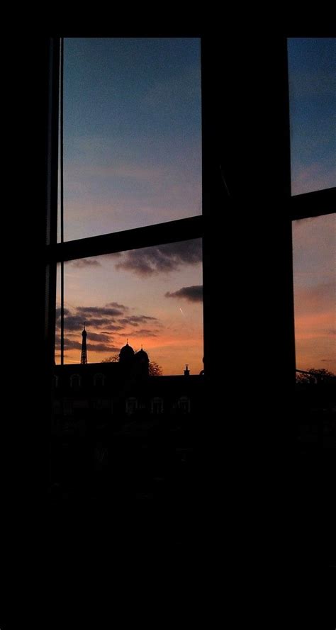 The Sun Is Setting Behind A Window With A View Of Some Buildings In The