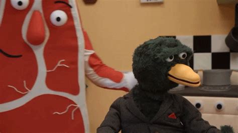 A Stuffed Bird Sitting On Top Of A Chair Next To A Person In A Suit