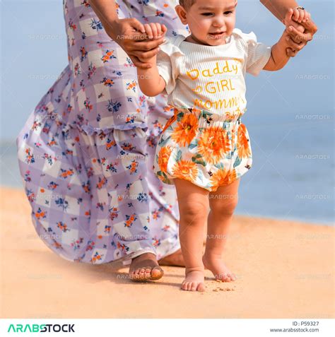 صورة مقربة لأم عربية خليجية سعودية تمسك إبنتها بحب وحنان، المشي على رمل شاطئ البحر، الاستمتاع