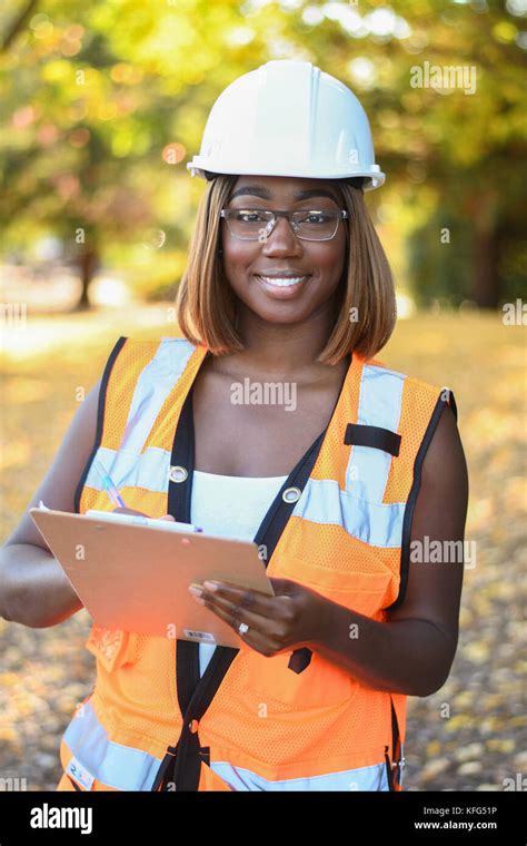 A Black Female Construction Worker Wearing A White Hat And Orange Vest