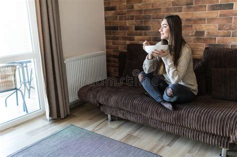 Cheerful Young Woman Eating Healthy Breakfast While Sitting On A Couch