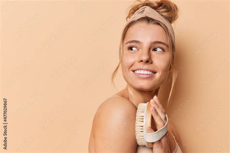 Sideways Shot Of Tender Cheerful Woman Uses Body Brush Stands Half