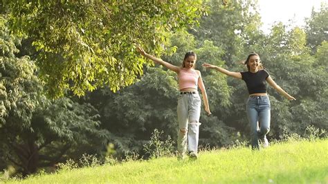 stock footage of two joyful female friends spreading their arms in the air and running in a park