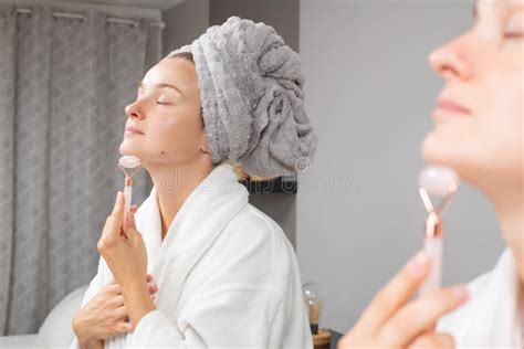 Beautiful Woman Is Getting Massage Face Using Jade Roller In Front Of The Mirror At Home Stock