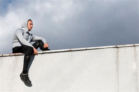 Free Photo Lateral View Man Sitting On A Wall And Looking Away