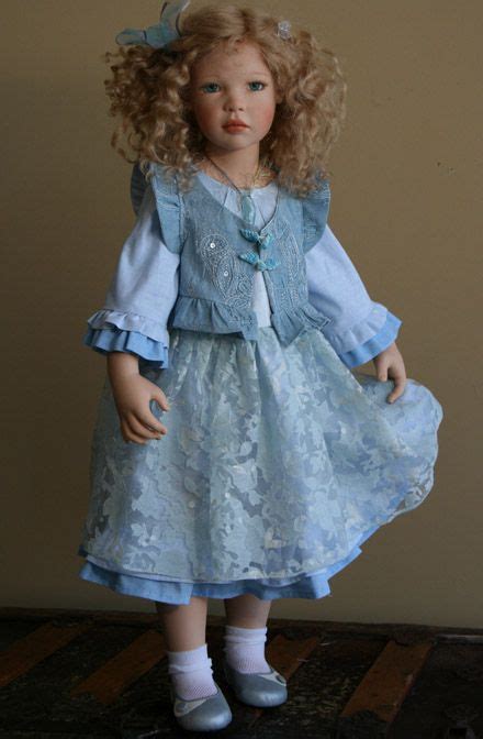 a doll with blonde hair wearing a blue dress and white shoes is standing on a wooden floor