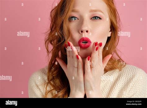 A Red Haired Curly Haired Girl With Red Lips Blows A Kiss While Looking