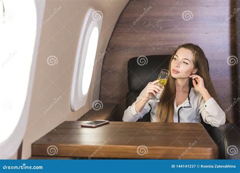 Young Attractive Female Businessman In A Private Jet Is Drinking Champagne From A Glass While