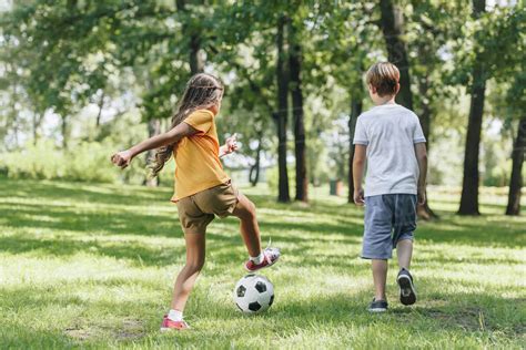 Back View Of Children Playing With Soccer Ball In Park Stock Photo