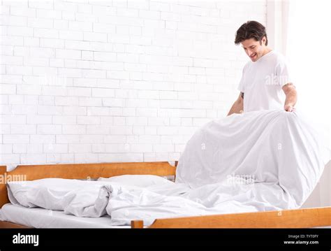 Millennial Guy Making Bed In Morning Domestic Chores Concept Stock