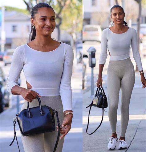 A Woman In White Top And Grey Leggings Holding A Black Handbag While Walking Down The Street