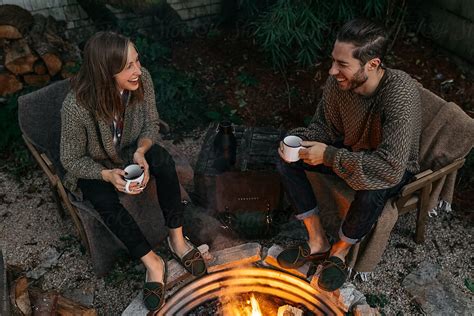 Young Couple Drinking Coffee Beverage Outdoors By Evening Fire In Back