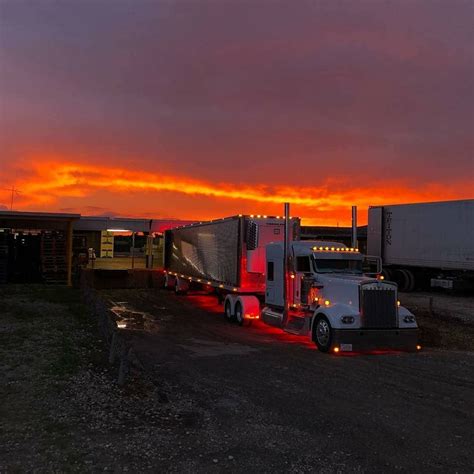 Two Semi Trucks Parked Next To Each Other In A Parking Lot At Dusk With