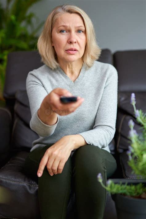 adult woman at home sitting on the couch and watching tv she is holding a remote control stock