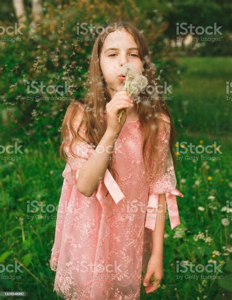 10 Year Old Teenager Girl Blows On A Dandelion Against A Background Of