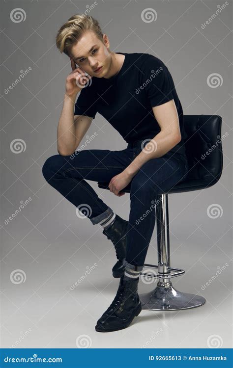 Full Length Picture Of A Young Male Model Sitting On A Chair Stock