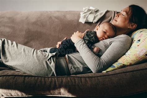 Madre Que Duerme En Un Sofá Con Su Bebé En Ella Imagen De Archivo