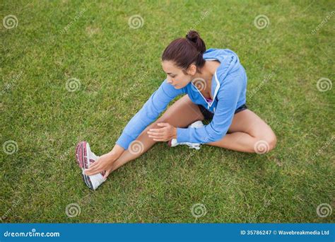 Sporty Woman Stretching Her Leg While Sitting On The Grass Stock Image