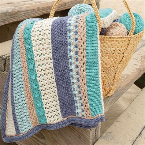 A Crocheted Blanket Sitting On Top Of A Wooden Bench Next To A Basket